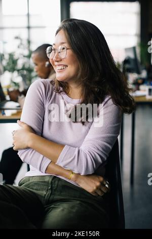 Happy businesswoman with arms crossed sitting in new office Stock Photo