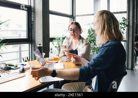 Young businesswoman discussing over laptop with colleague at desk in startup company Stock Photo