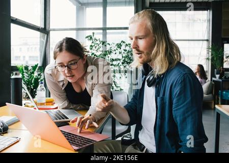 Female programmer discussing strategy with male colleague over laptop in new office Stock Photo