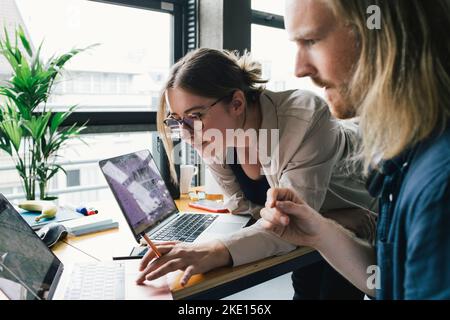 Businesswoman working on laptop with male colleague in startup company Stock Photo