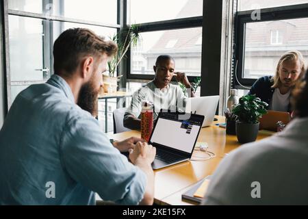 Businessman working on laptop by colleagues in tech-startup company Stock Photo