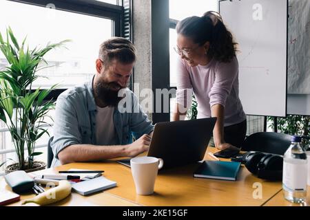 Cheerful male and female computer programmers discussing over laptop in new office Stock Photo
