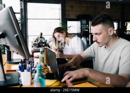Young businessman working on laptop by female colleague in office Stock Photo