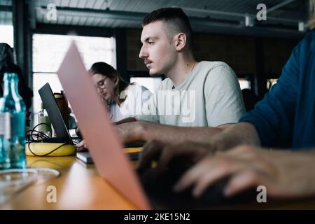 Concentrated businessman working on laptop amidst colleagues in startup company Stock Photo