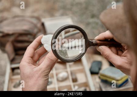 A man looks at a stone through a magnifying glass, close-up Stock Photo