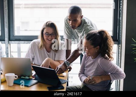 Smiling multiracial female and male computer programmers discussing over laptop in office Stock Photo