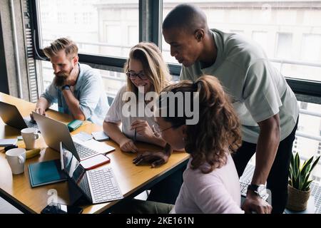 Multiracial female and male computer programmers discussing over laptop in startup company Stock Photo