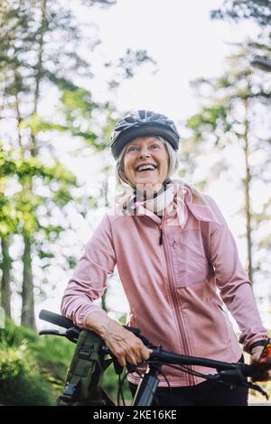 Smiling senior woman looking away while standing with cycle Stock Photo
