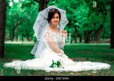The bride sits in the park with an umbrella in her hand Stock Photo