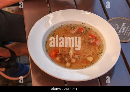 Bojnice, Slovakia - 06.11.2022: Soup with noodles and vegetables in a white plate on a wooden table. Stock Photo