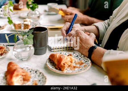 Hands of senior woman writing in diary at cafe Stock Photo