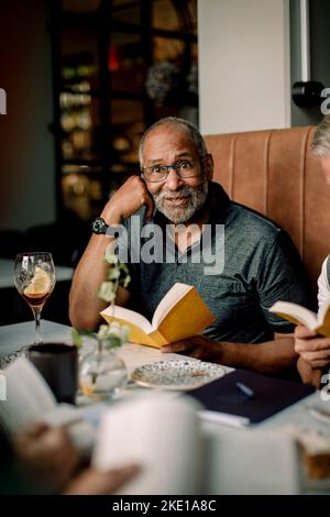 Senior man wearing eyeglasses sitting with book in cafe Stock Photo