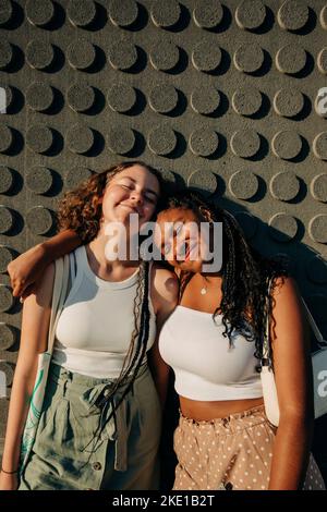 Smiling teenage girl with arm around female friend standing against wall Stock Photo