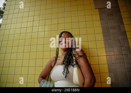 Low angle view of happy teenage girl with braided hair standing against yellow wall Stock Photo