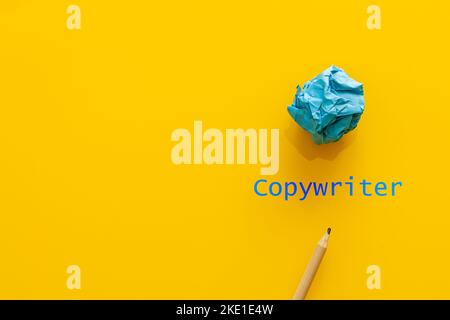 Blue text copywriter on a yellow background, next to a pencil and a crumpled piece of paper, a symbol of a failed text, Concept of a copywriter's crea Stock Photo