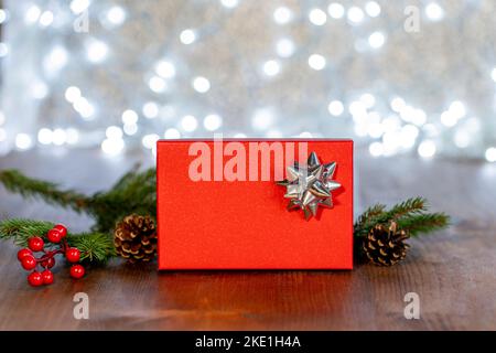 Red gift box with a silver ribbon on a bokeh background of white lights and Christmas decorations. Stock Photo