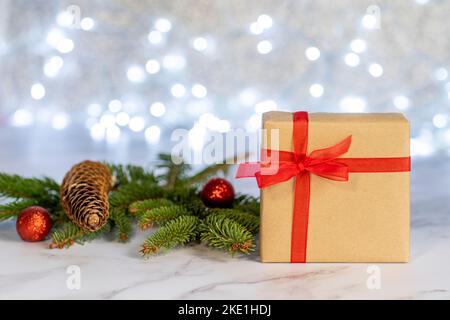 Gift box with a red bow on a bokeh background of white lights with various Christmas decorations. Stock Photo