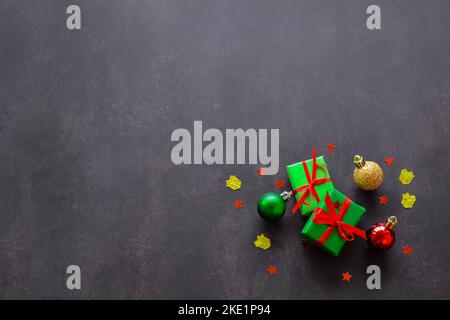 Gifts in green paper with red and yellow ribbons, gold, red and green christmas balls and confetti in the form of red stars. Black background, copy sp Stock Photo