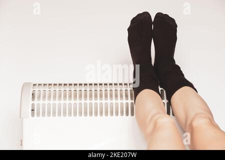 Women's legs in socks on an electric convector on a white background, a warm house, a heater Stock Photo