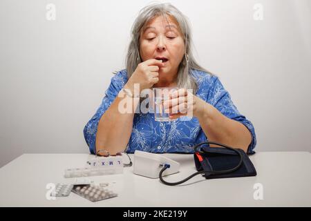 older white-haired woman taking a pill after having her blood pressure checked Stock Photo