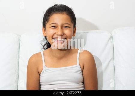 portrait of latin brunette girl, sitting on the sofa smiling and showing her teeth, girl with indian features Stock Photo