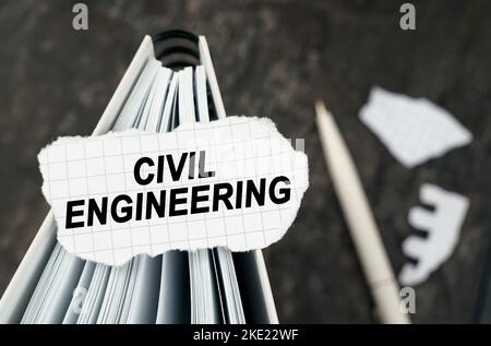 On the table is a notebook on which lies a piece of torn paper with the inscription - Civil Engineering. The pen lies outside the sharpness zone. Stock Photo