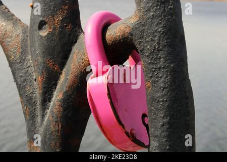 A pink lock in the shape of a heart close-up hangs on a rusty lattice. wedding tradition. The concept of love and fidelity. Stock Photo