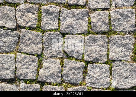 Texture of paved stone road with asymmetrical stones with sprouted grass at seams. Top view Stock Photo