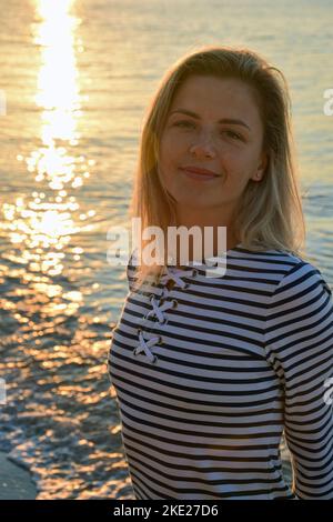 Young beautiful white woman in a striped dress on the background of the waves of the evening sea Stock Photo