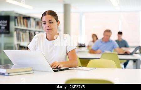 Portrait of woman studying at library using books and laptop Stock Photo