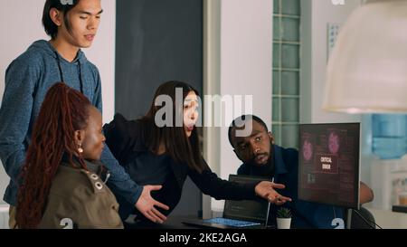 Diverse team of coders dealing with security breach alert on computer, trying to solve hacking and critical error. Engineers using terminal window and having system hacked crash. Stock Photo