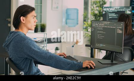 Asian programer developing database interface and writing server code, working in software development office. System engineer creating algorithm on terminal window. Handheld shot. Stock Photo