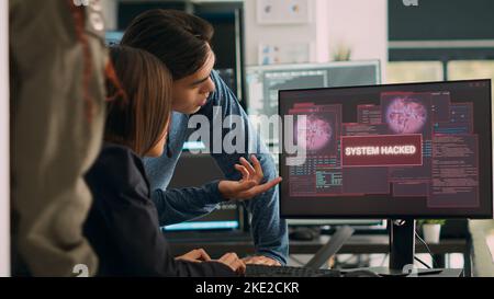 Asian software programer having system crash hacking problem with security breach warning, writing code on multiple screens. Showing critical error message and hacked pc server. Handheld shot. Stock Photo