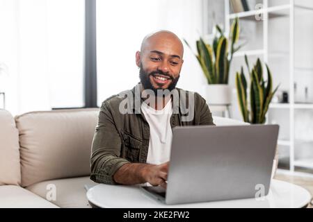 Home office concept. Happy mature man working on pc laptop, sitting on comfy sofa at home and smiling, free space Stock Photo