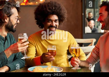 Close up portrait of cheerful man looking at camera and smiling while holding a beer in a bar. Stock Photo
