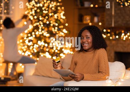 Young Man Using Tablet A young African American woman decorates a red holiday gift in a cozy ...