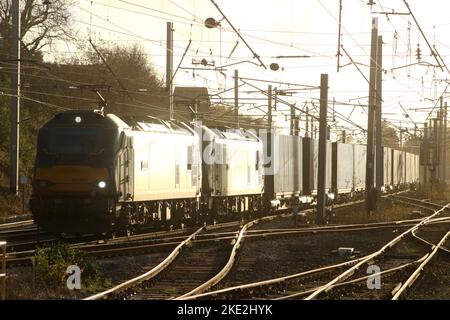 Sunlight reflecting off the side of a double headed container train as it passes through Carnforth on West Coast Main line on 9th November 2022. Stock Photo