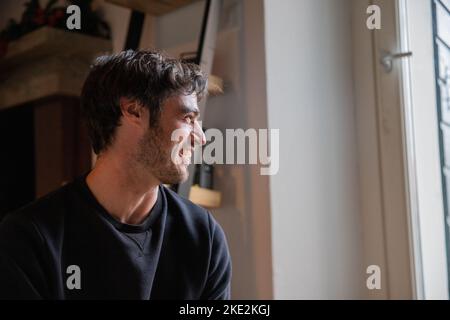 Headshot of a smiling young caucasian man in his 30s looking at the window in his room. Stock Photo