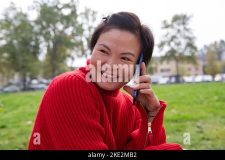 Smiling dimpled beautiful chinese woman talking at the cellphone at the park. Stock Photo