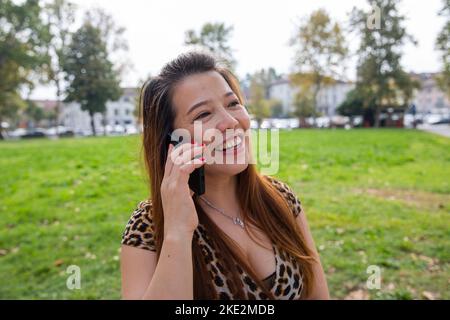 Attractive chinese woman in her forties chatting at the phone in a public park. Stock Photo