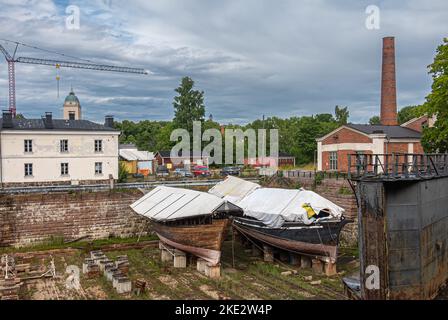 Helsinki, Finland - July 19, 2022: Suomenlinna Fortress. Viaporin historic shipyard dry dock with 2 old worn boat hulls on blocks covered by white tar Stock Photo