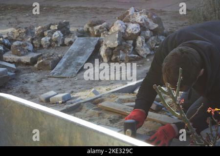 Defocus paver master. Man lays paving stones in layers. Garden brick pathway paving by professional paver worker. Worker installing concrete paver blo Stock Photo