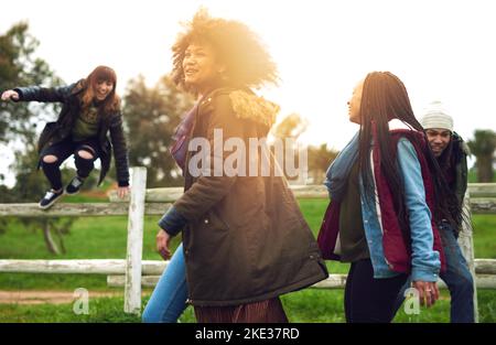 We bring fun to everything we do. a group of friends jumping over a fence in a field for fun. Stock Photo