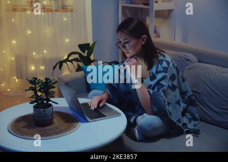 Tired focused woman using laptop at night while working overtime against christmas lights background Stock Photo