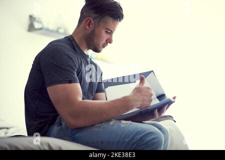 If you want it, youll work for it. a confident young man studying some paperwork while sitting on his bed at home. Stock Photo