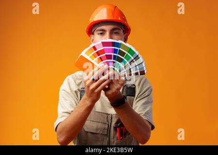 Handsome young worker in uniform holding paint samples palette on yellow background Stock Photo