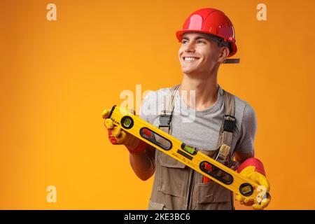 Young male handyman holding construction spirit level on yellow background Stock Photo