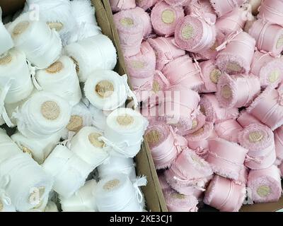 White and light pink silk ribbons with wooden spools a lot in store. Texture background. Selective focus Stock Photo