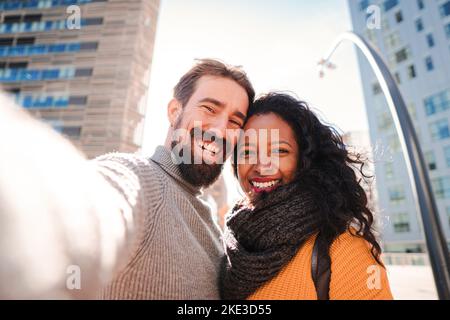 Portrait of smiling young multiethnic couple taking selfie photo with a mobile phone while doing a trip. Travel concept. Stock Photo