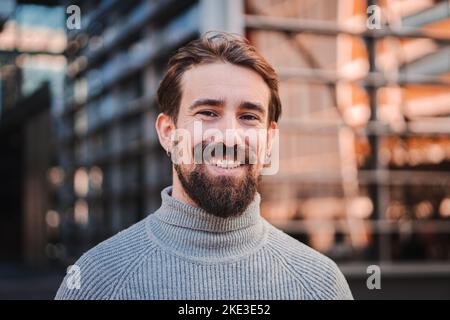 Close up portrait of awesome young caucasian male smiling and looking at camera at the background city office buildings Stock Photo